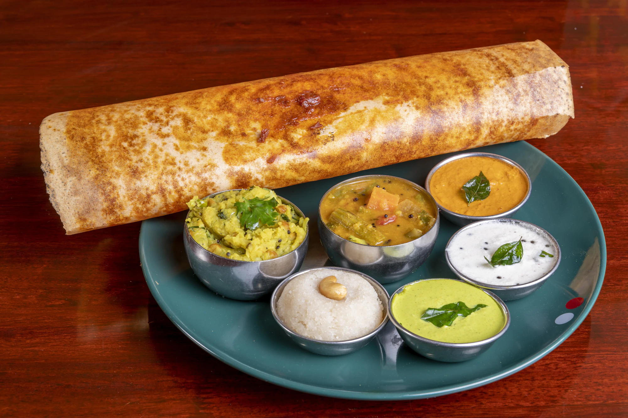 Rolled masala dosa with chutneys and sambar in steel bowls