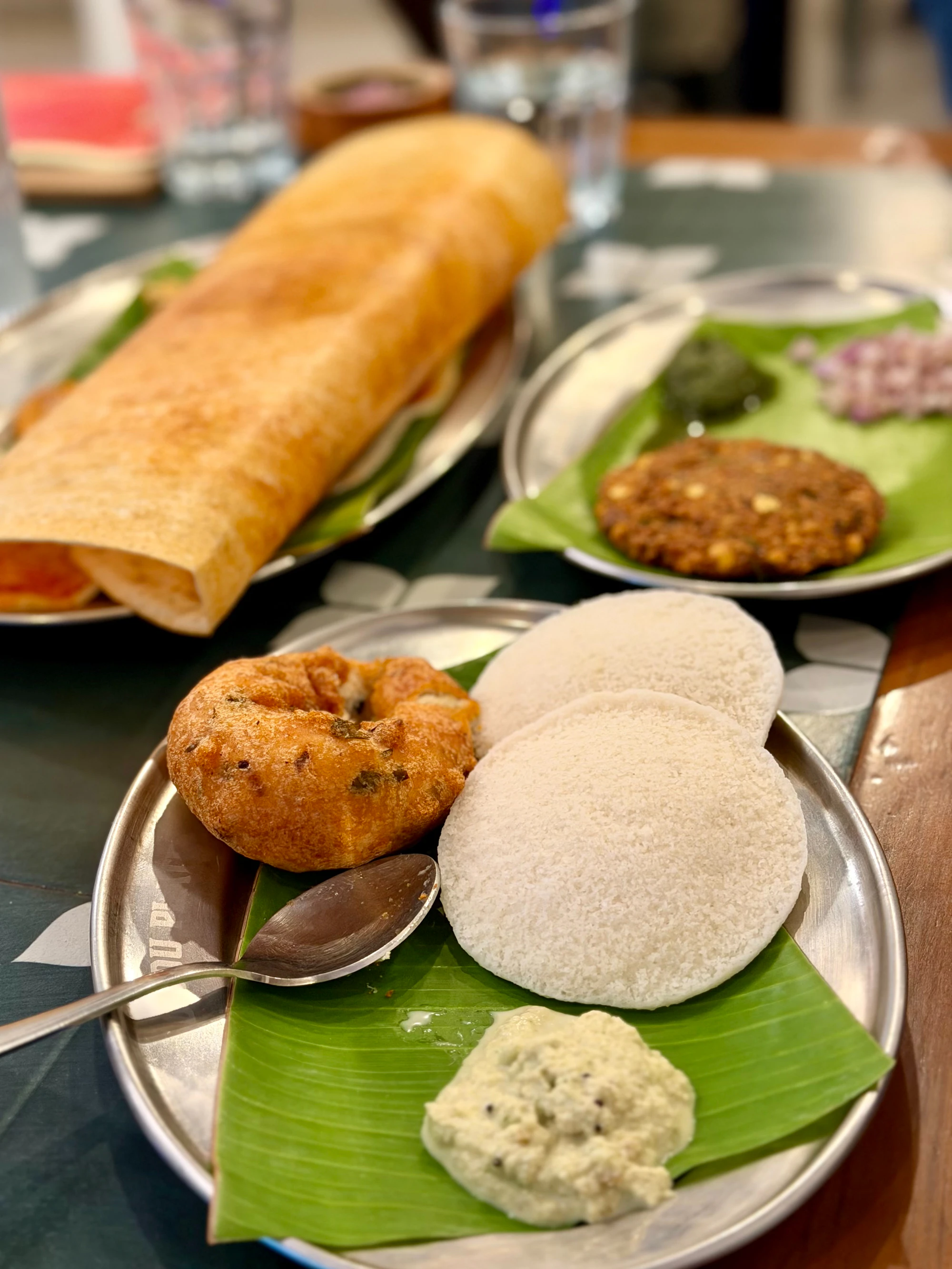 Idli, vada and dosa with coconut chutney on a steel plate lined with banana leaf
