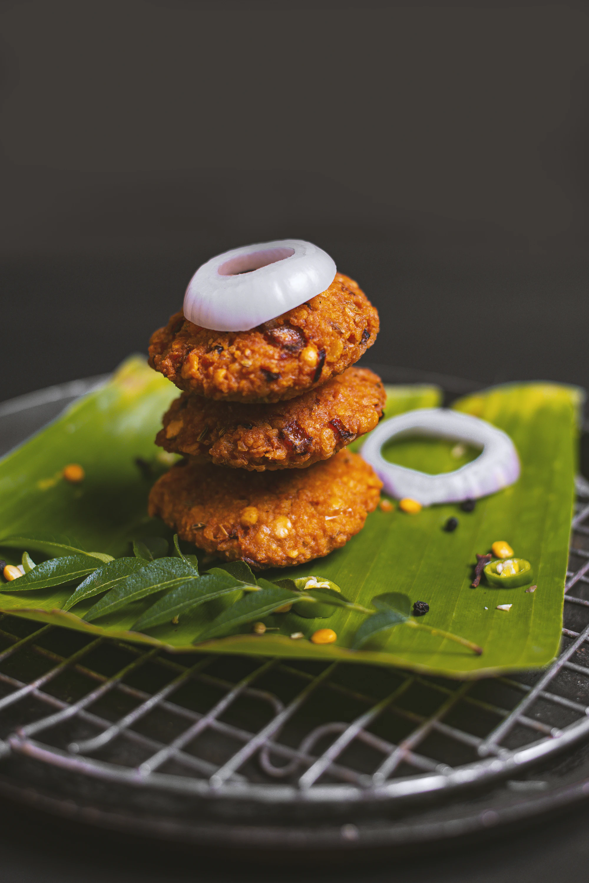 Stack of three lentil vadas with onion rings on a banana leaf