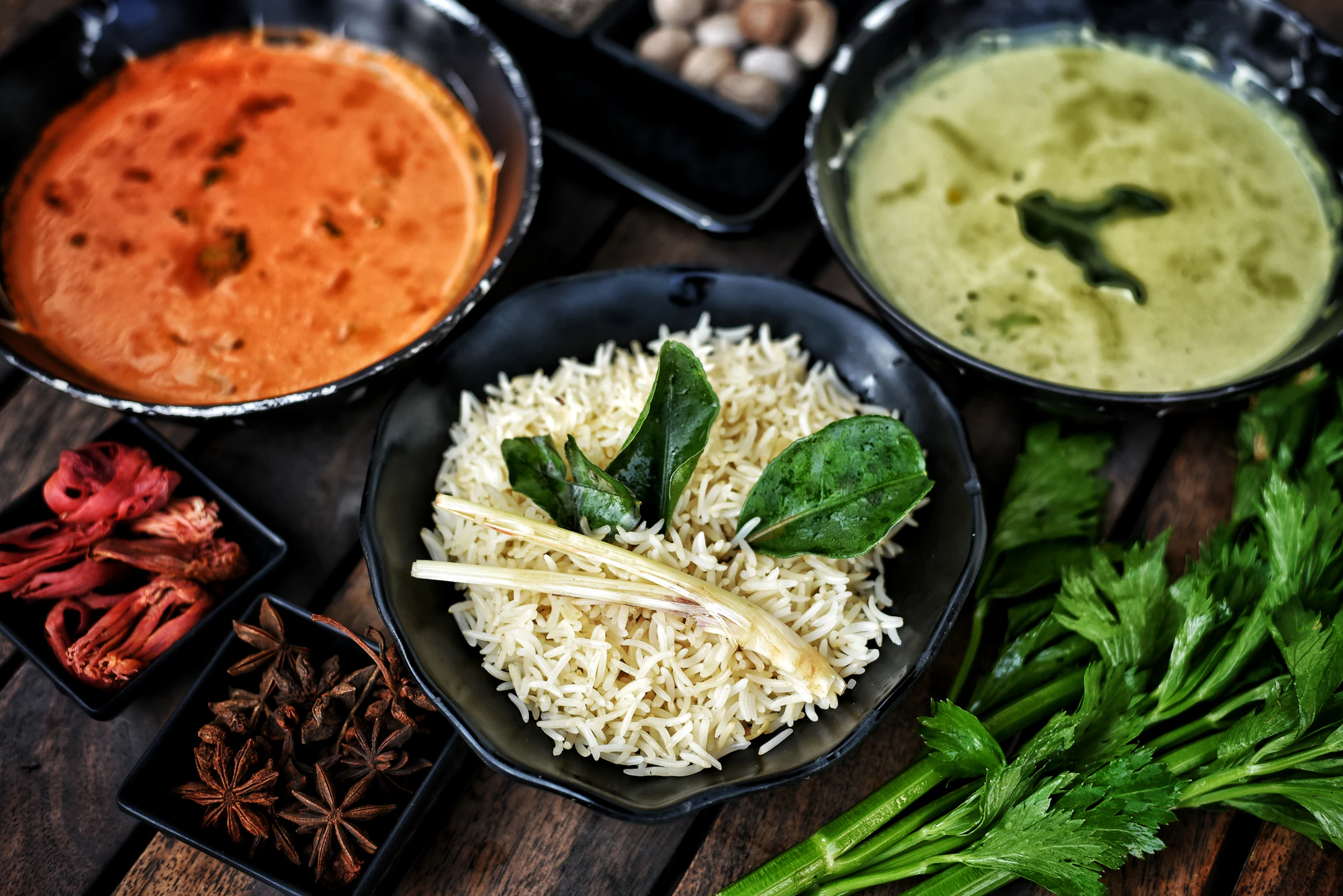 Bowls of curry, rice and whole spices on a dark table