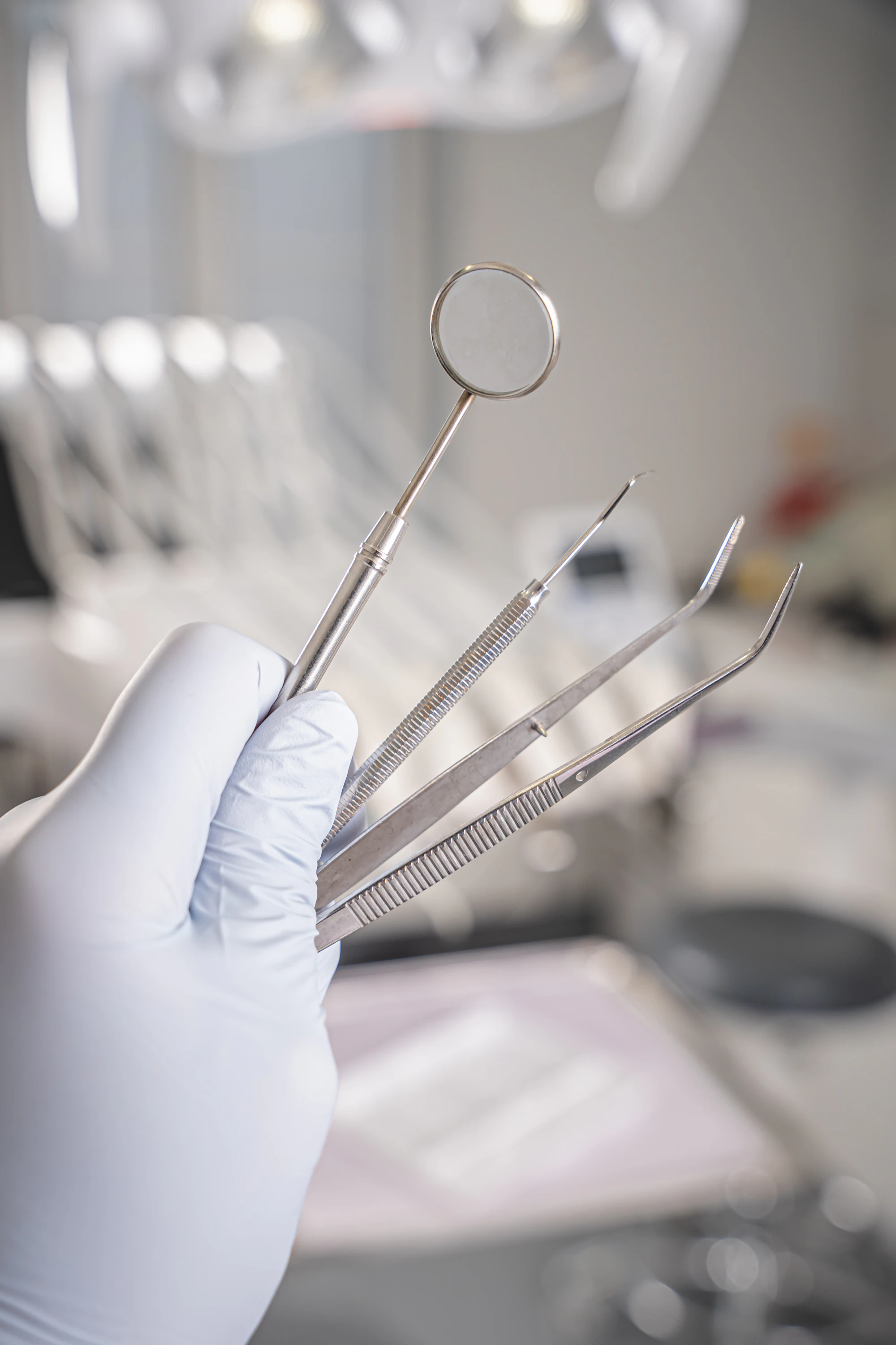 A gloved hand holding a dental mirror and probes
