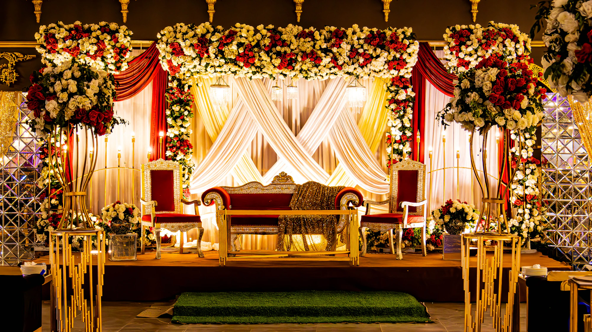 A reception stage with red and white flowers, draped fabric and a gold sofa