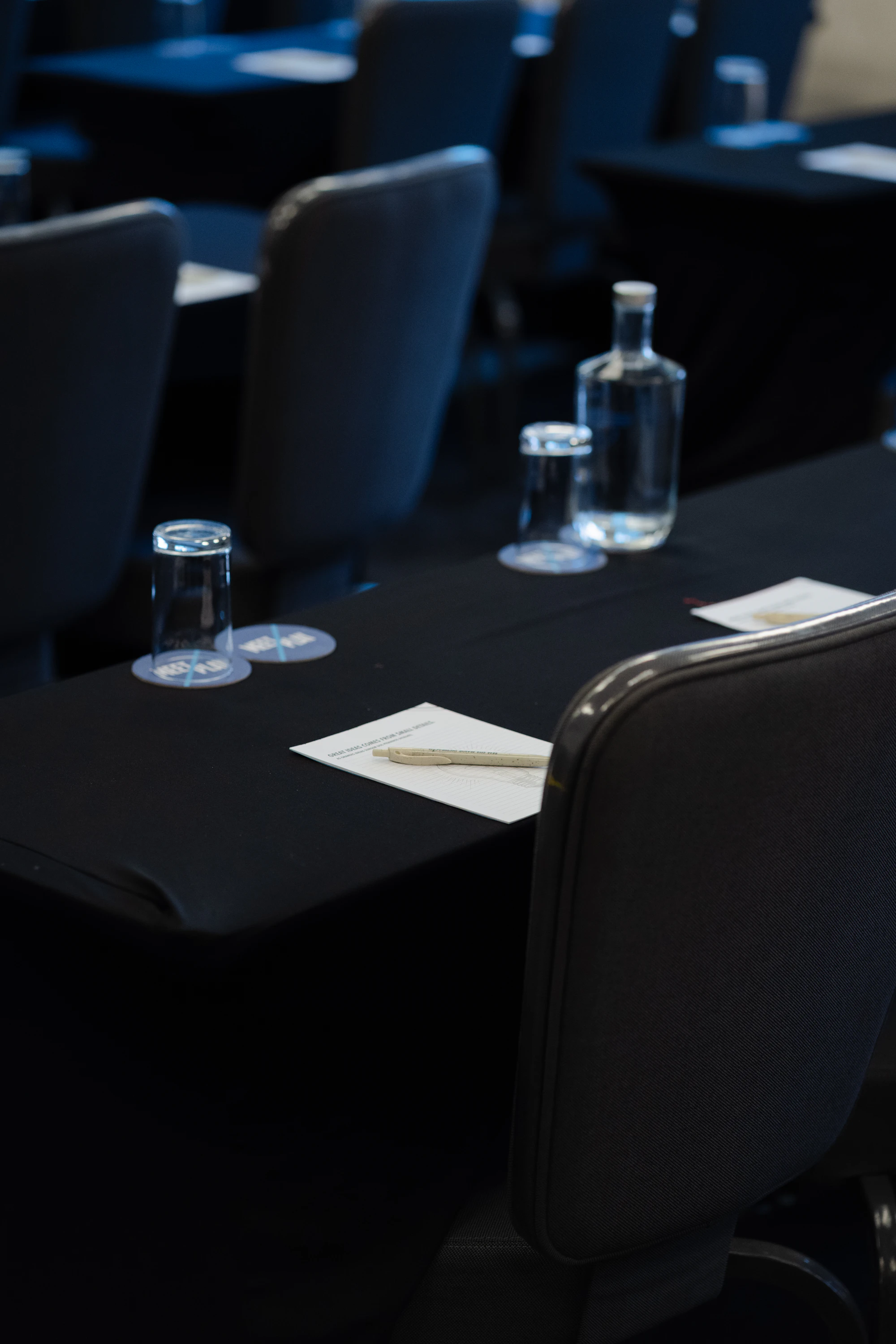 A conference room with dark tables, notepads and water bottles set out
