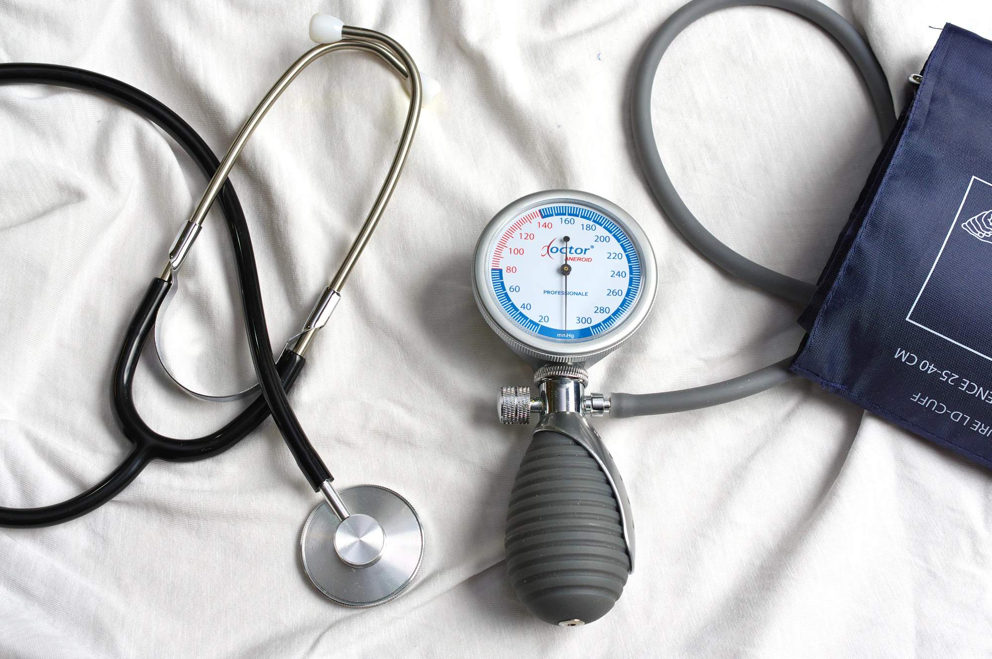 A stethoscope and a blood pressure cuff laid out on a white sheet