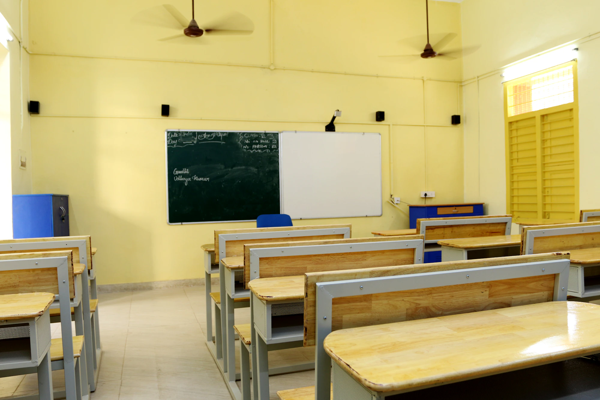 A bright yellow classroom with wooden benches, a blackboard and a whiteboard