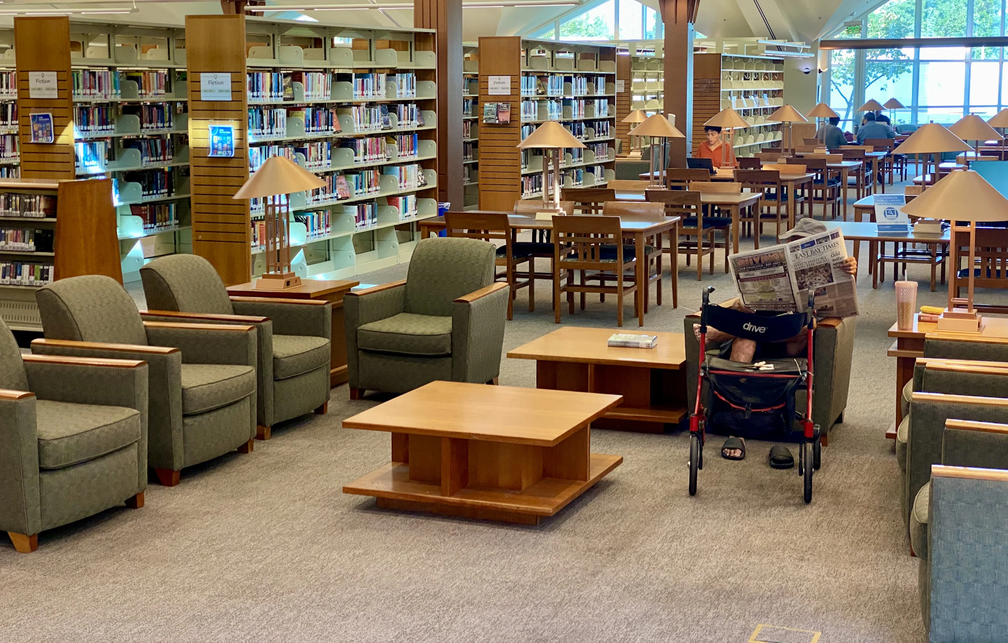 A library reading area with armchairs and low tables in front of tall bookshelves