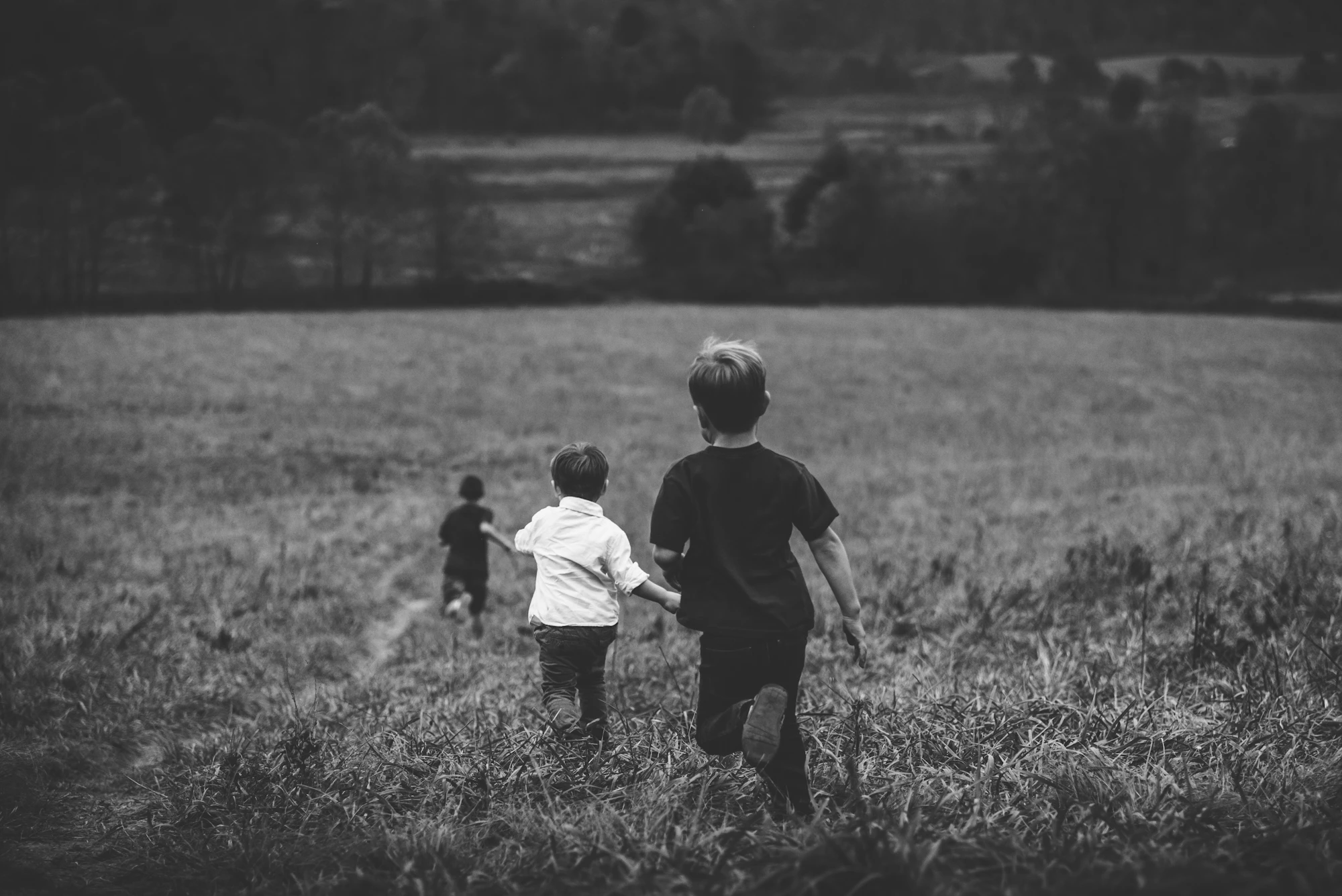 Three boys running across a grassy field, seen from behind, in black and white