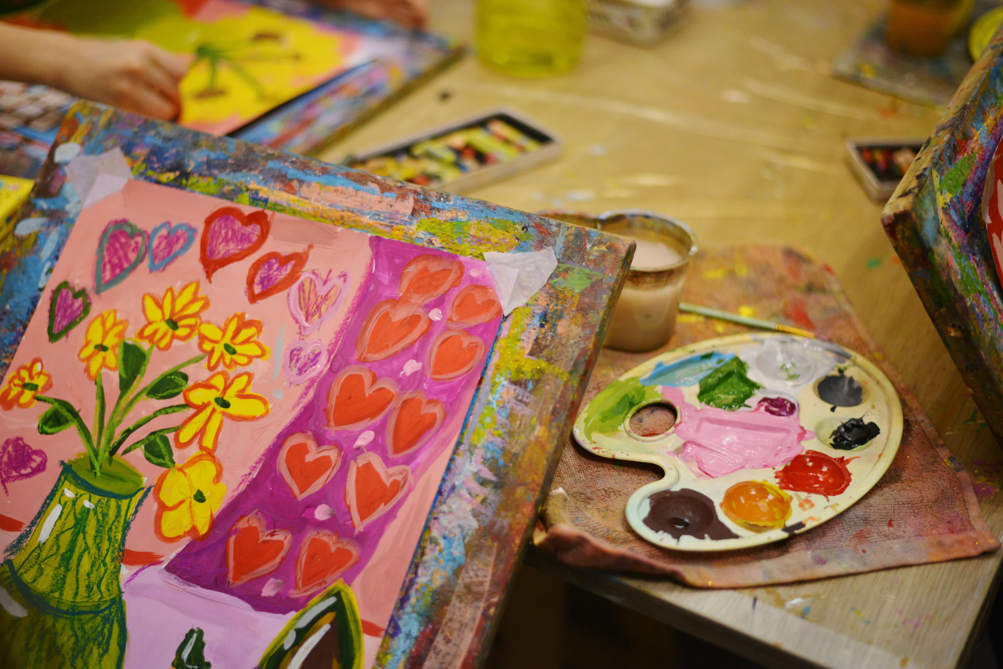 A colourful flower painting and a paint palette on a table covered in art supplies
