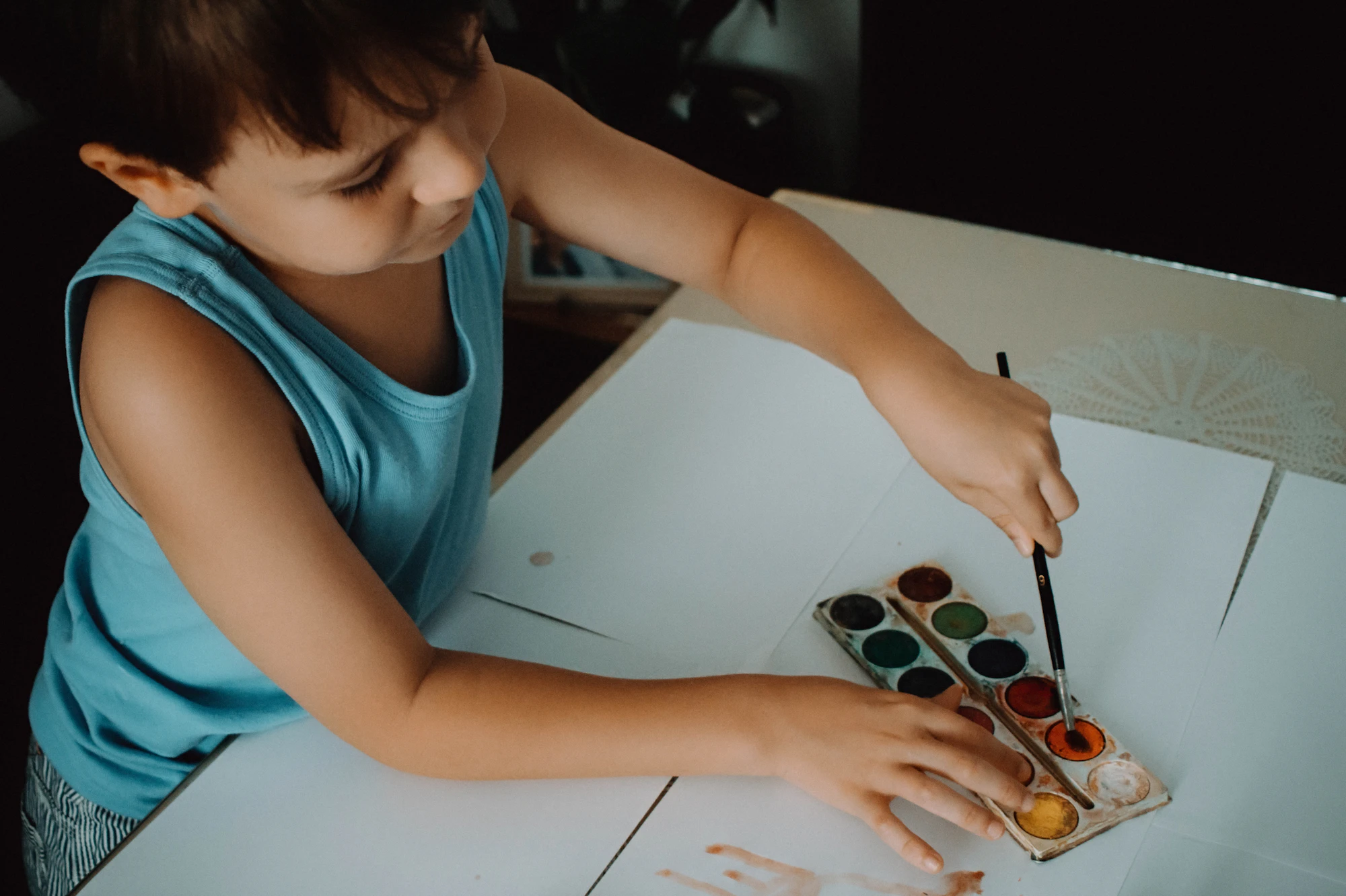A young child painting with a watercolour set at a white table