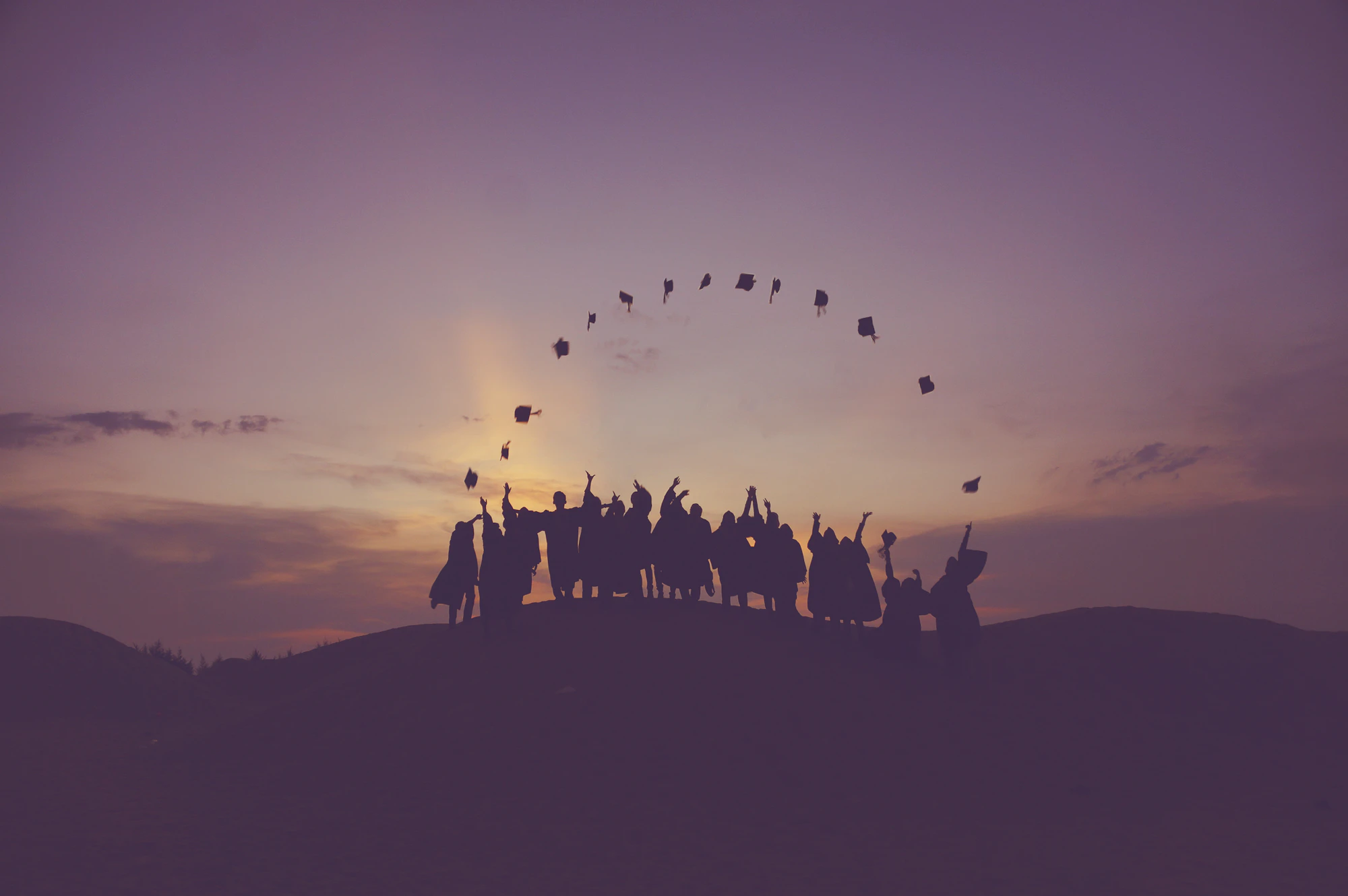 Silhouettes of graduates throwing caps at sunset