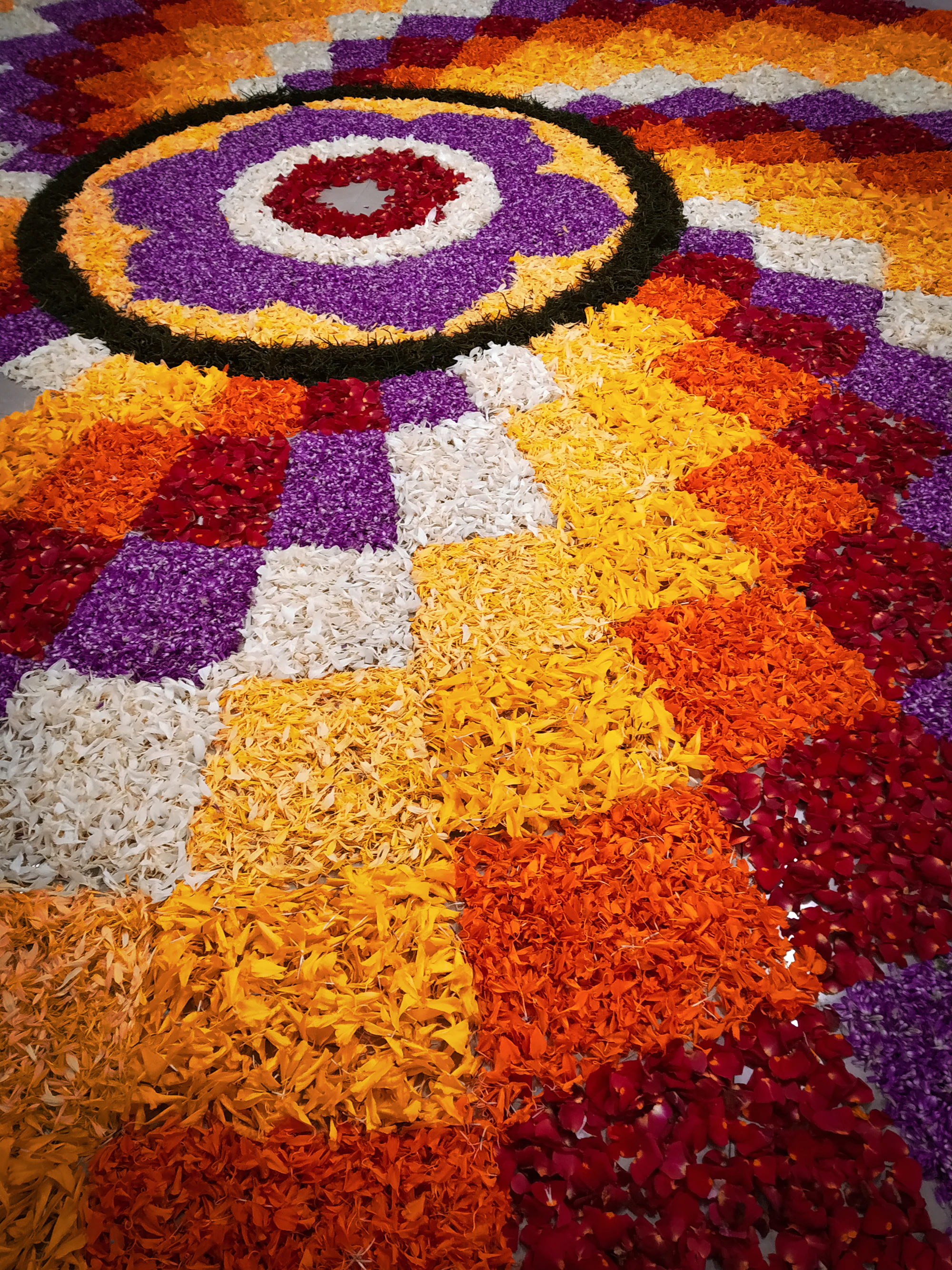 A close-up of an Onam pookalam made of red, orange, yellow and white petals