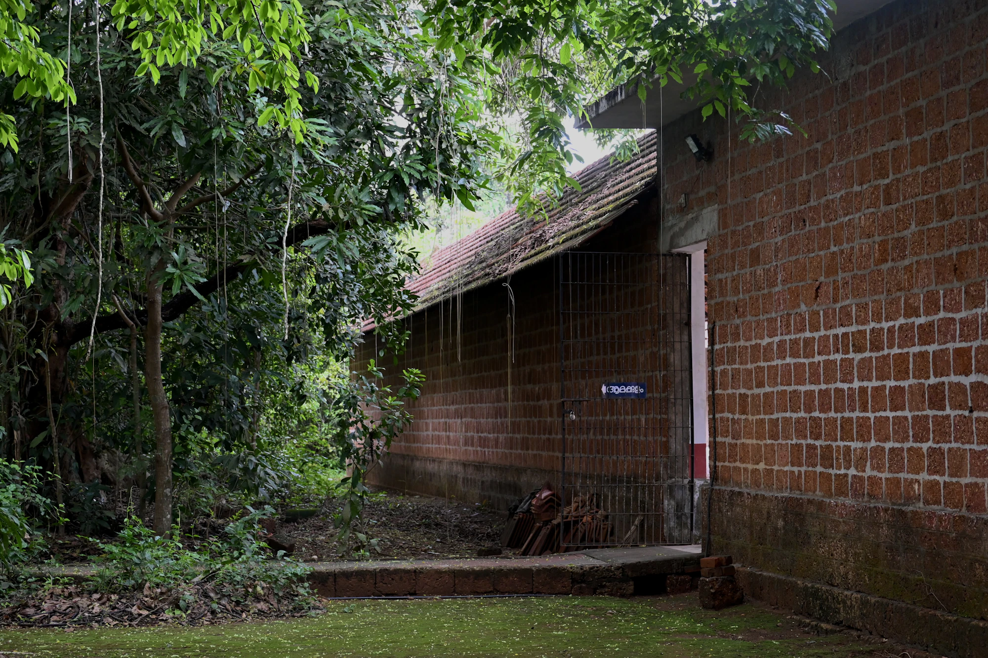 A laterite brick building with a tiled roof among trees and grass