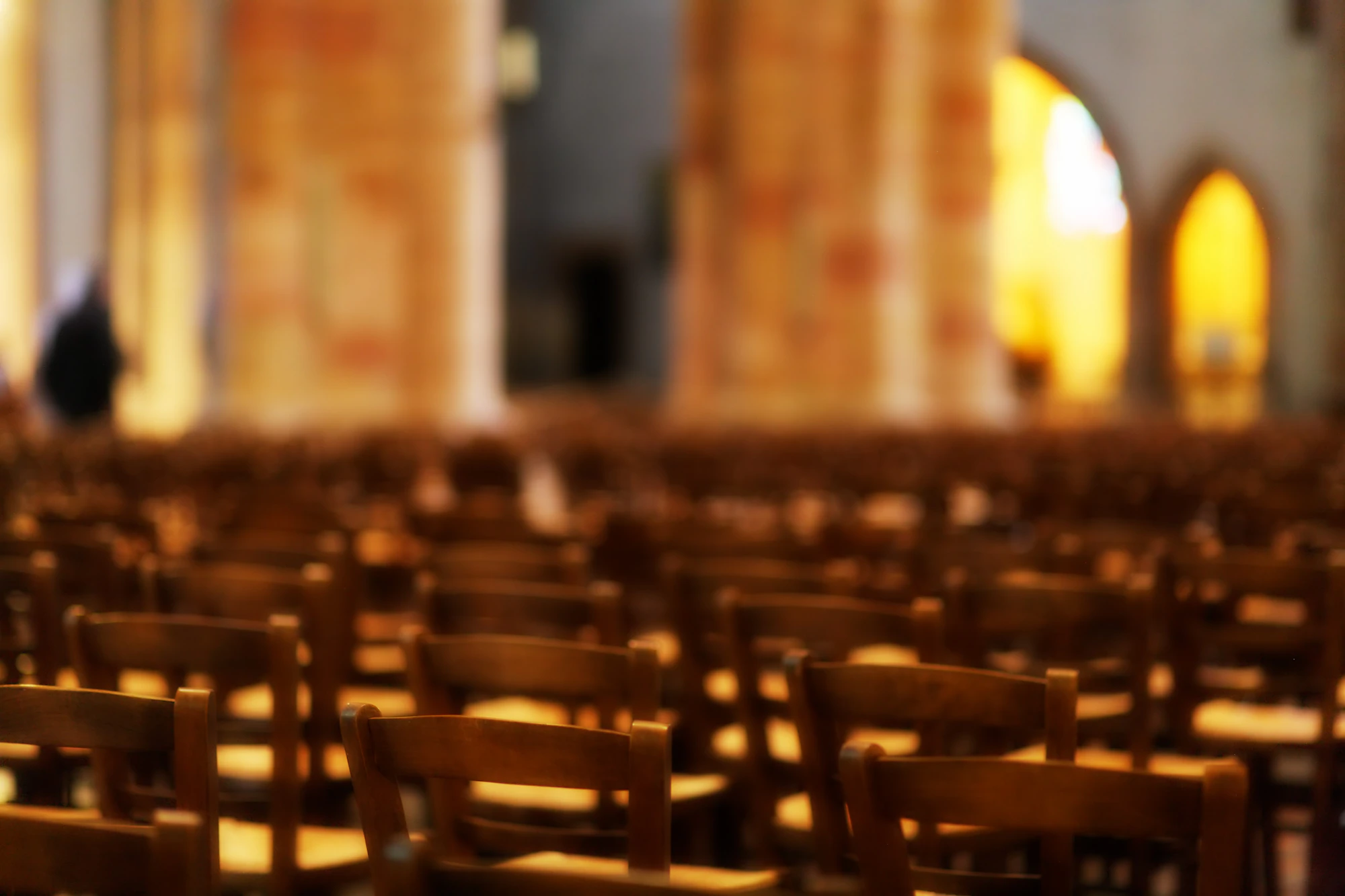 Rows of empty wooden chairs in a warmly lit hall