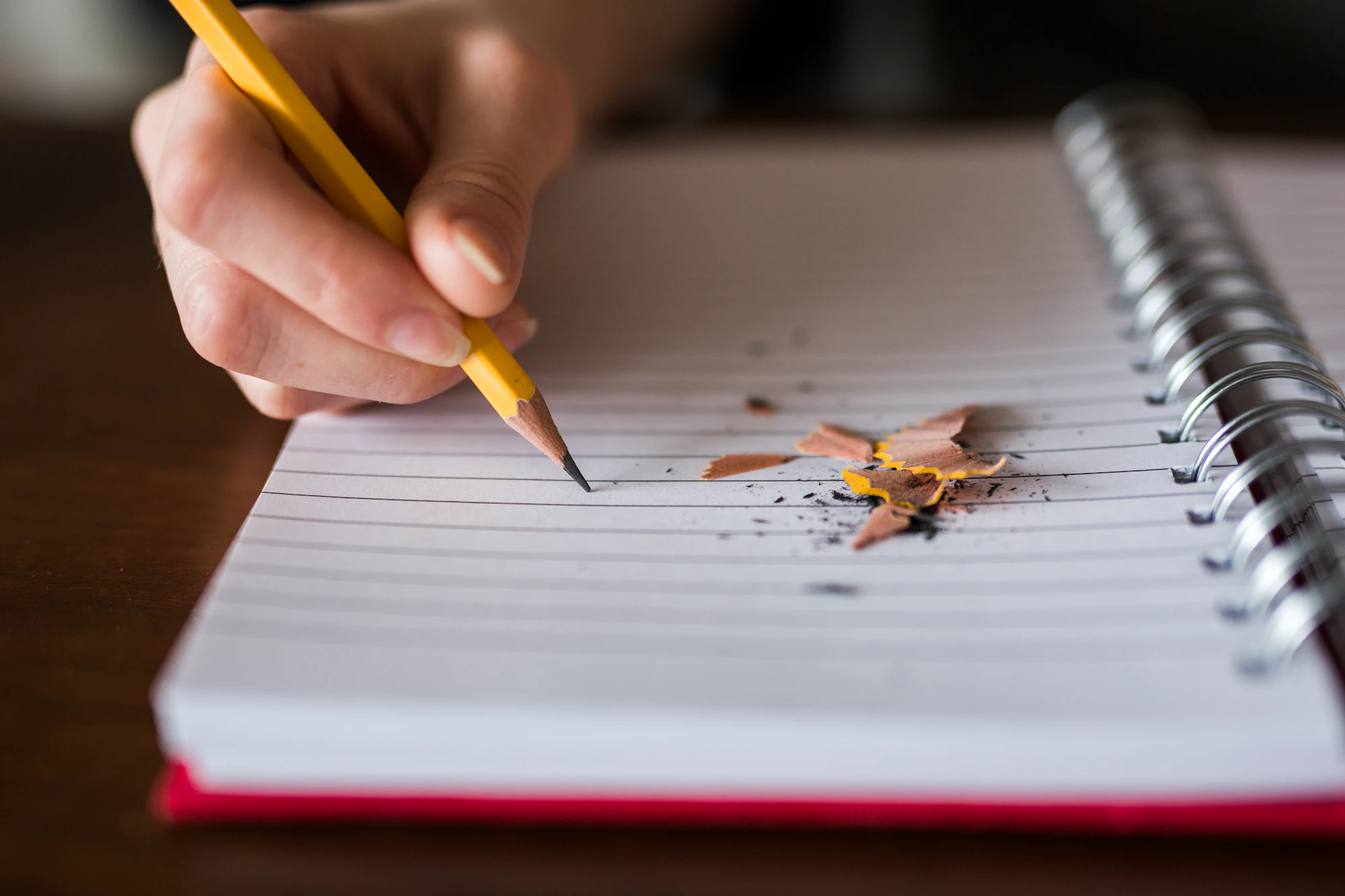 A hand writing with a pencil in a spiral notebook