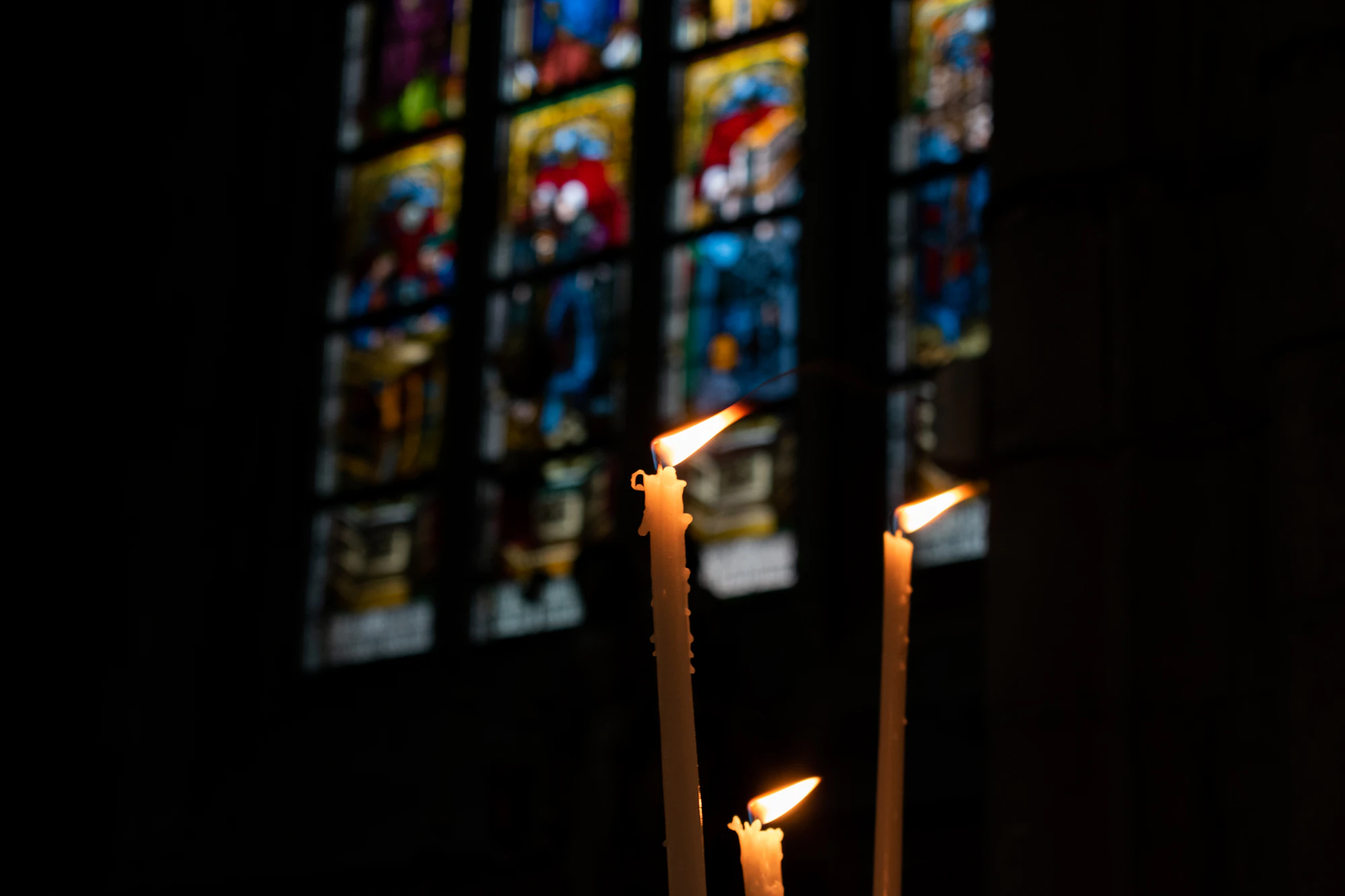 Three candles in front of a stained glass window