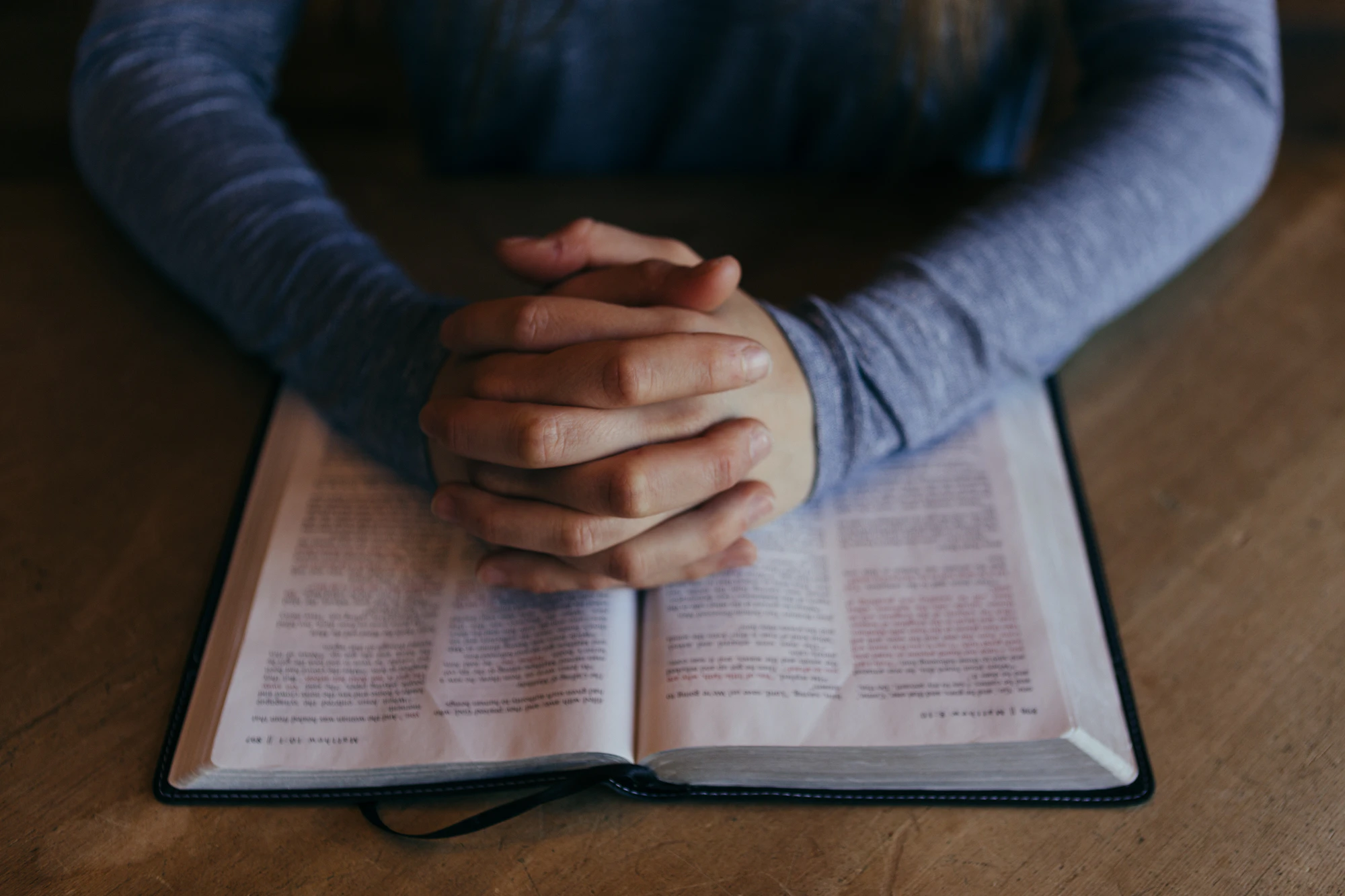 Folded hands resting on an open Bible
