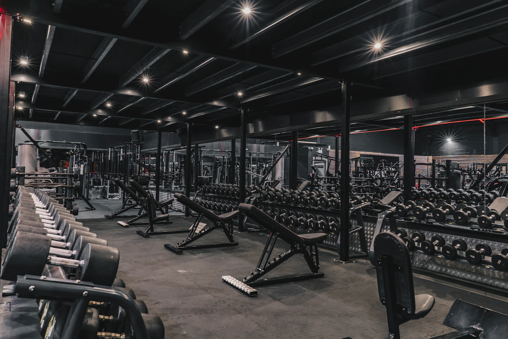 A dark gym floor with racks of weights and benches