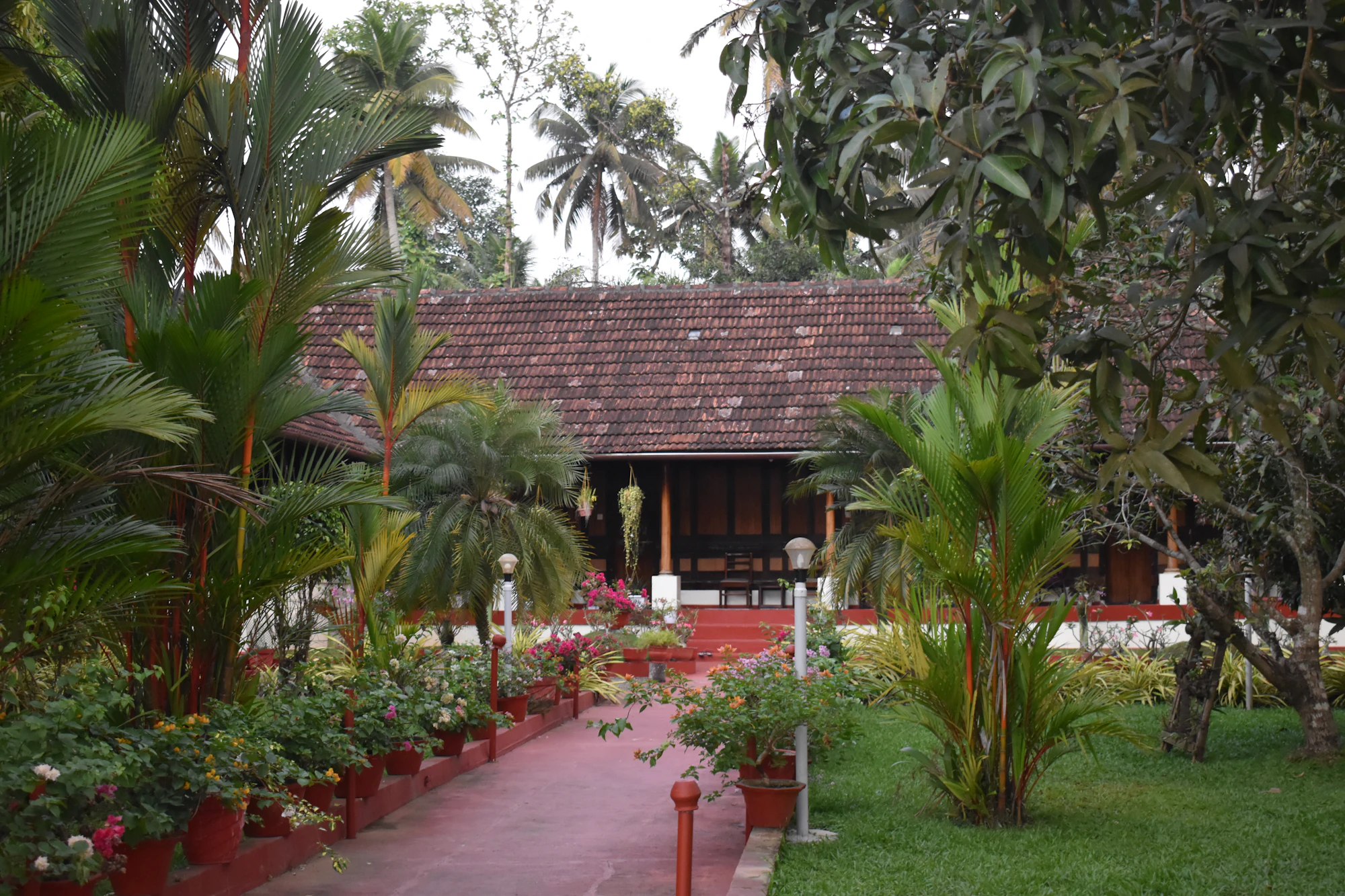 A tiled-roof house behind a garden of palms and flowers