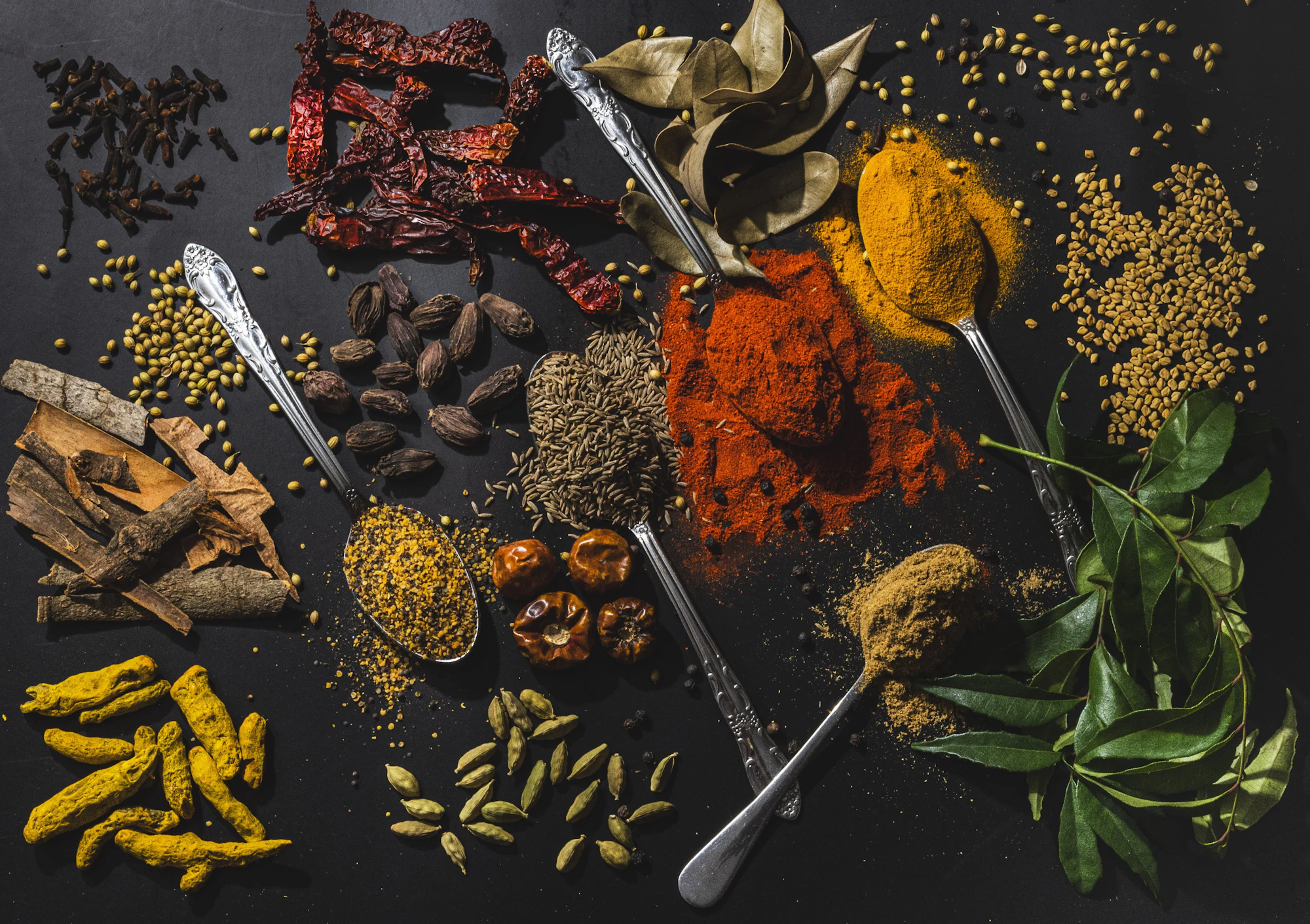 Whole and ground spices with curry leaves on a dark table