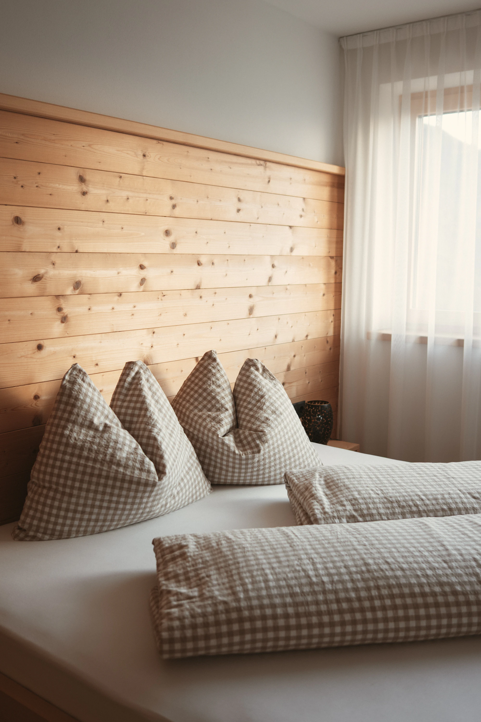 A bed with checked pillows against a wooden headboard