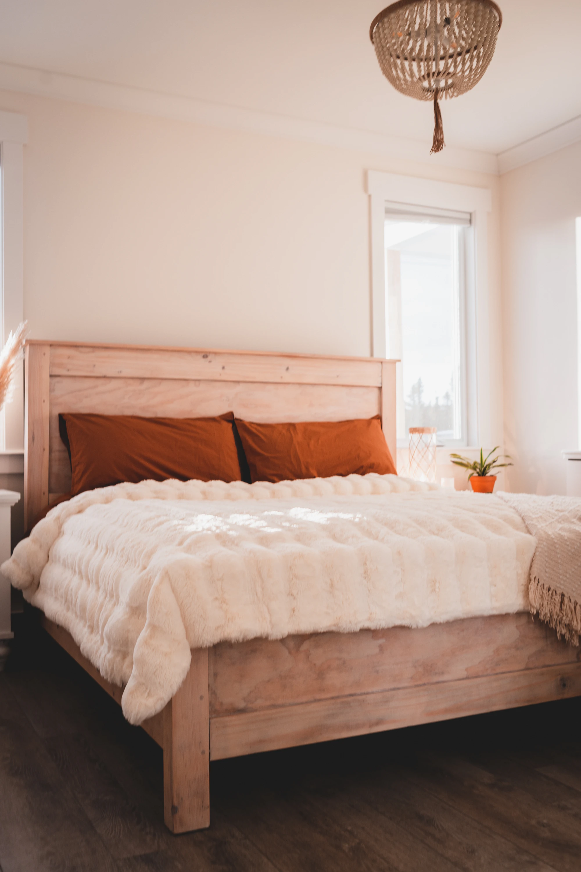 A simple wooden bed with white linen and rust cushions