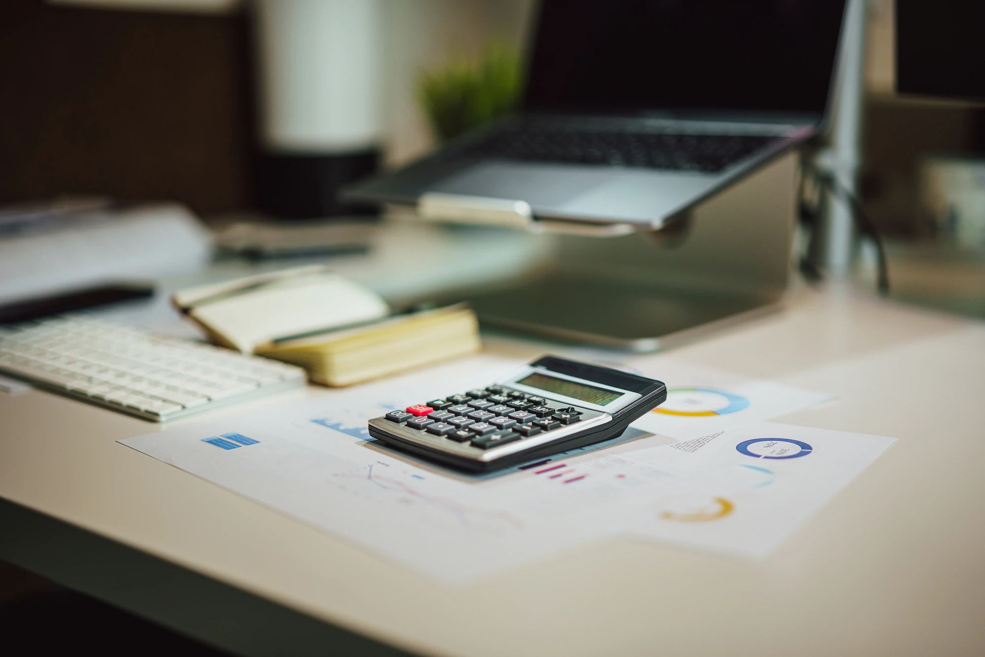 Calculator and printed charts on a desk beside a laptop