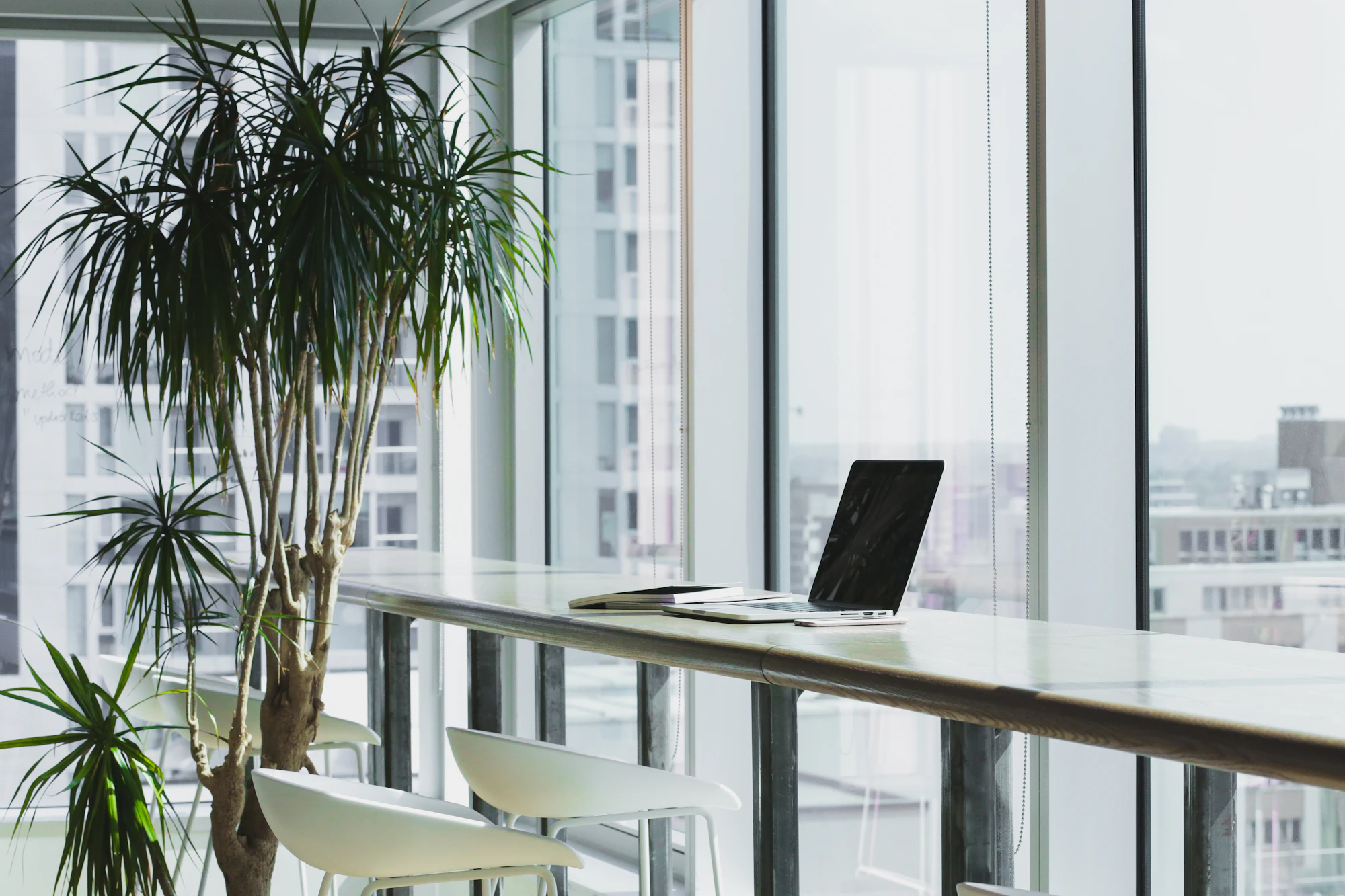 Laptop on a long white desk by tall office windows