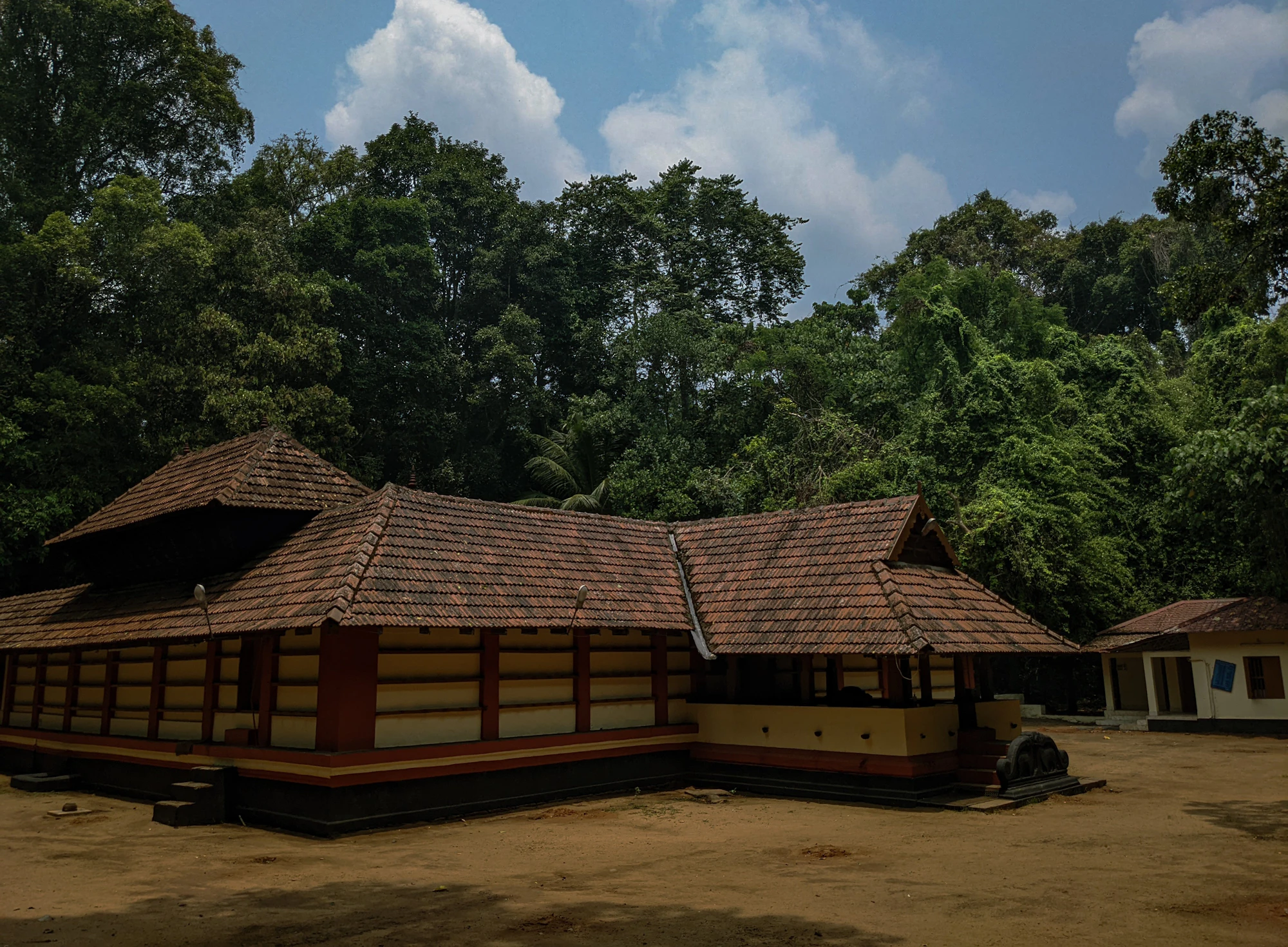 Long traditional building with sloping tiled roofs beside a forest
