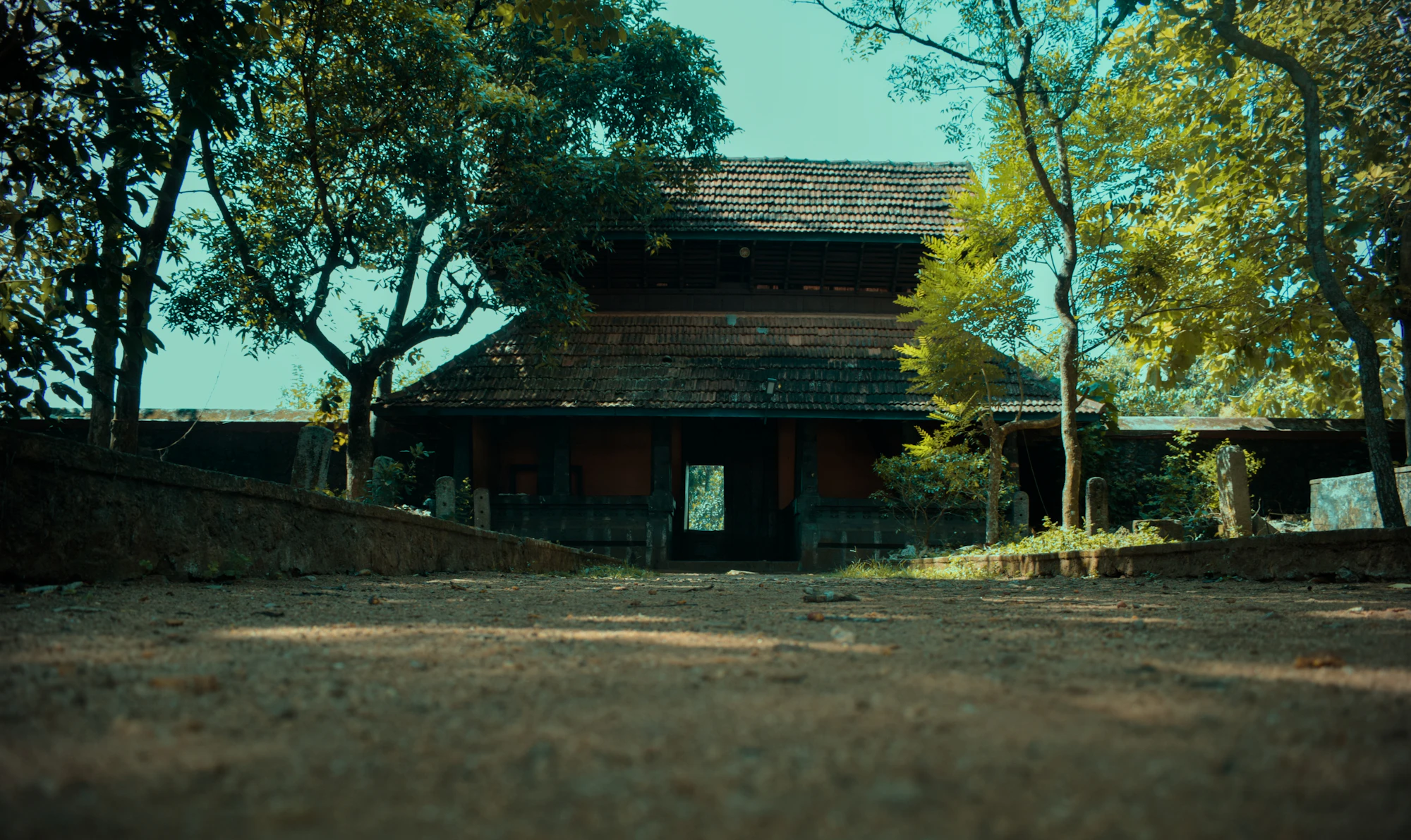 Traditional wooden building under trees with a dusty courtyard
