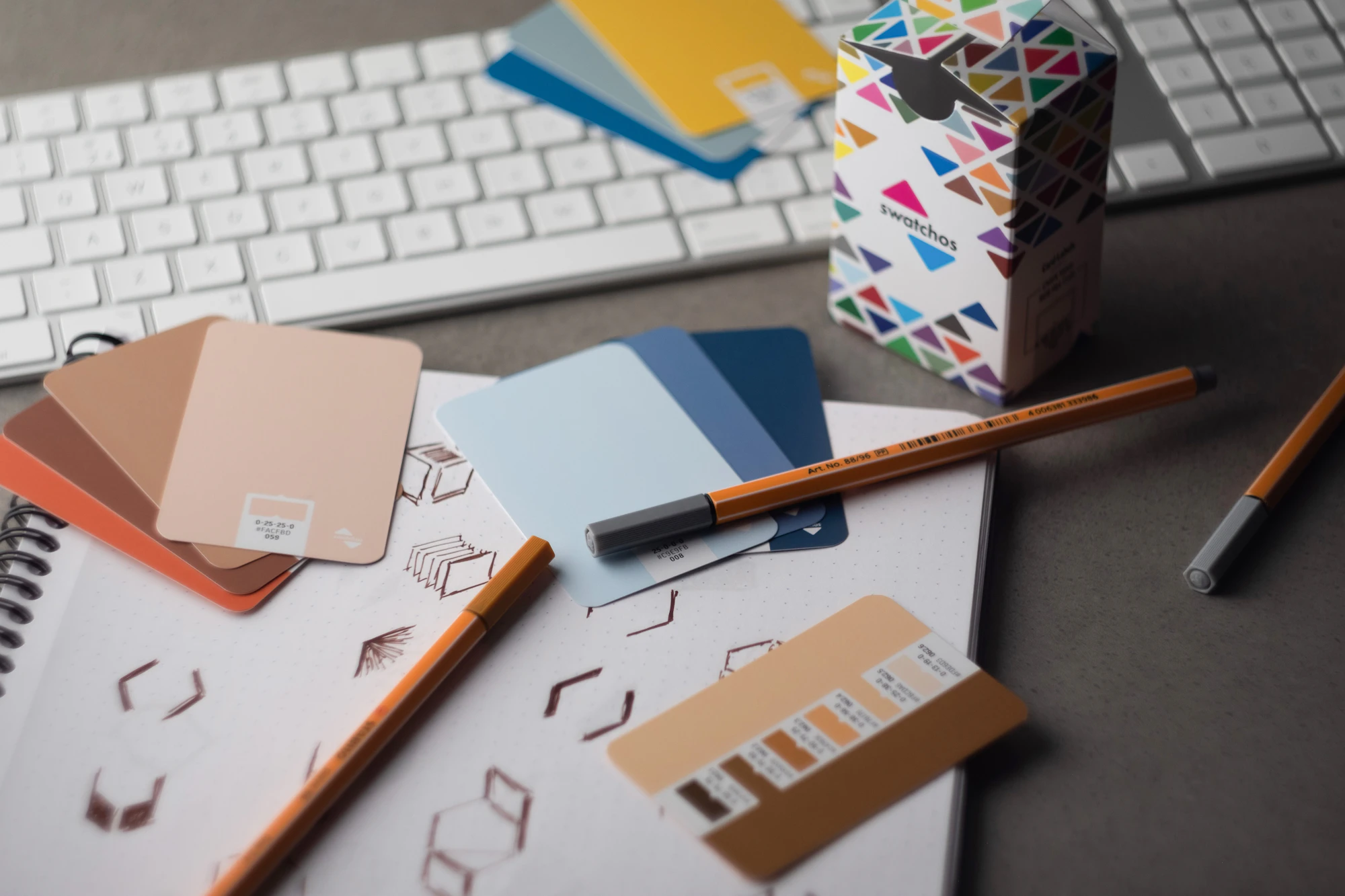 Colour swatches, pencils and sketches on a desk beside a keyboard